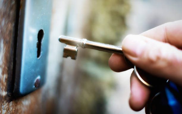 A hand holds a key on  a key ring, about to lock or unlock an old wooden door.